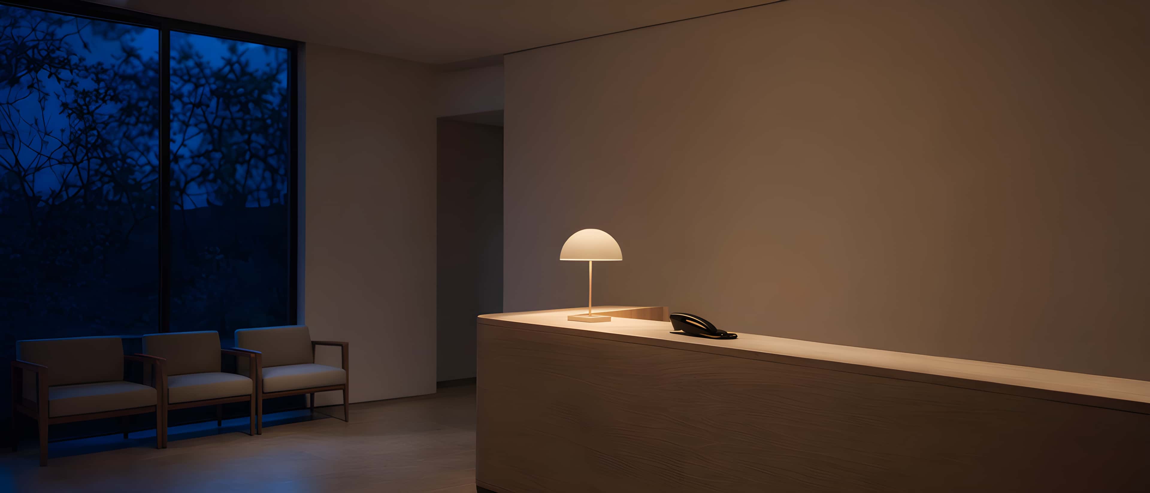 An empty practice reception at dusk, one lamp lit, the phone waiting on the desk